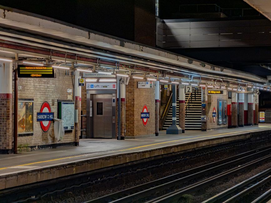 An outdoor view featuring the iconic Big Ben clock tower positioned behind a black and red London Underground sign with a white and black circle, prominently displaying the word 'UNDERGROUND.' Below t